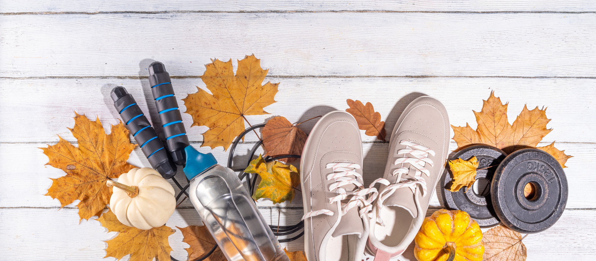 Autumn sport fitness background. Outdoors fall workouts concept. Running sneakers, dumbbell barbell discs, jump rope, water bottle, wooden background, with autumn leaves, pumpkins top view copy space